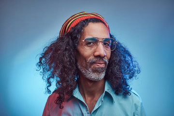 Smiling African Rastafarian male wearing a blue shirt and beanie. Studio portrait on a blue...