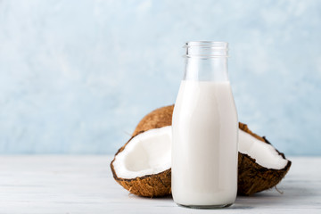 Health content, coconut milk in a glass bottle, coconut halves, light wooden table, close-up