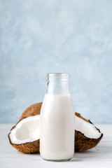 Health content, coconut milk in a glass bottle, coconut halves, light wooden table, close-up, vertical