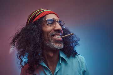 Happy African Rastafarian male smoking cigarettes. Isolated on a blue background.