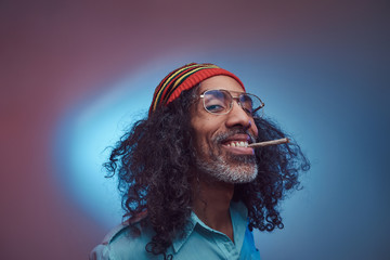 Happy African Rastafarian male smoking cigarettes. Isolated on a blue background.