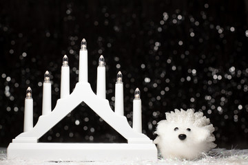 Christmas white candle lights bridge and white hedgehog decoration on dark background with silver color bokeh. Holiday concept