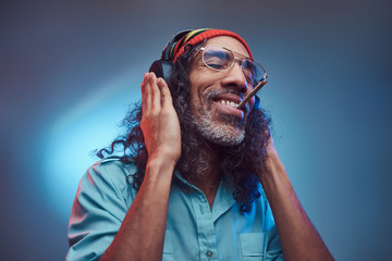 Studio portrait of African Rastafarian male enjoys music in headphones and smoking weed. Isolated...