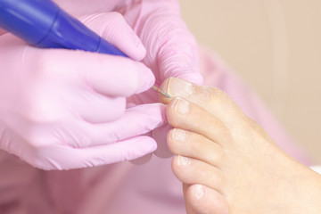 Professional hardware pedicure using an electric machine. Patient at the pedicure procedure. polishing the nail plate, processing the cuticle using a pedicure machine.