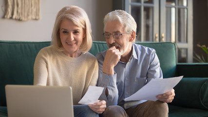Elderly couple sitting on couch holding bills use computer