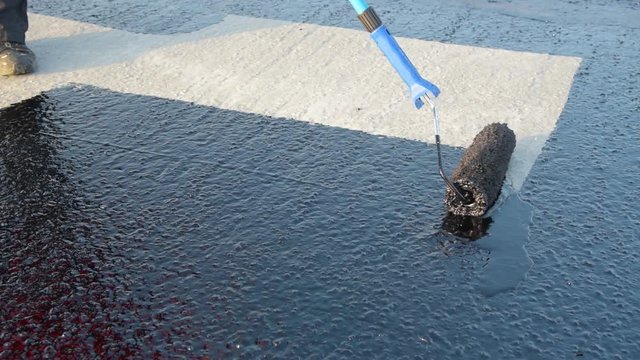 Waterproofing coating. Worker applies bitumen mastic on the foundation. Roofer cover the rooftop polymer modified bitumen waterproofing primer, with a roller brush.