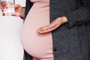 Close-up of young pregnant woman holding glass of water and pill. Concept of pregnancy, health care, gynecology, medicine and healthy lifestyle. Mother waiting of the baby. 