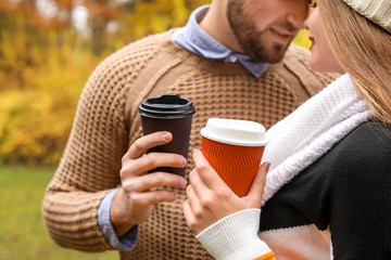 Loving young couple with cups of coffee in autumn park, closeup