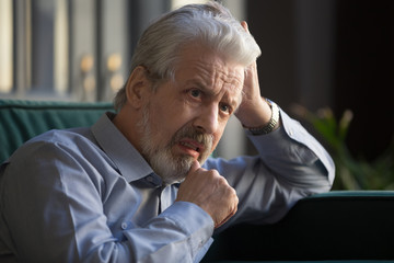 Pensive serious elderly man thinking sitting on couch