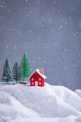 Miniature wooden red house on the snow over blurred Christmas decoration background, toned, snowflakes effect