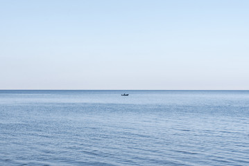 Obraz premium Lone fisherman in a boat with a motor on the water in the middle of a lake or sea