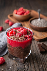 Superfood healthy vegan dessert, dark cocoa chia seed pudding with raspberry puree, topped with fresh berries and chocolate shavings in a glass jar
