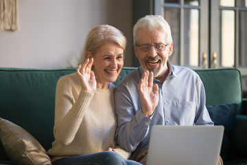 Fototapeta premium Aged couple looks at computer screen wave hands greeting friend