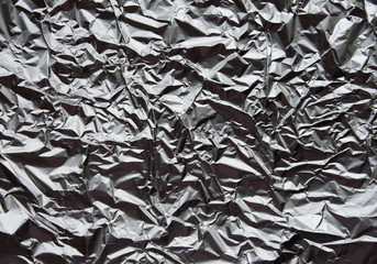 Crumpled silver aluminum foil closeup background texture. Abstract metallic paper holographic...
