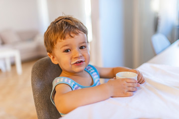 Adorable boy drinking milk or yogurt. Cute baby boy with milk mustache, indoor portrait. Eat healthy. Toddler having snack. Healthy nutrition. Drink milk. Boy cute baby eating breakfast.