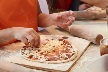 The kid 's learning to make pizza from the dough.