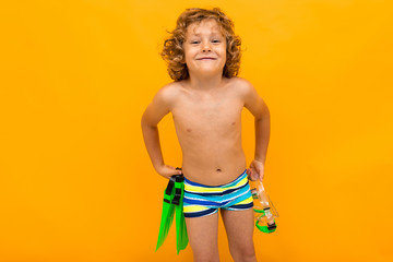 Red-haired curly boy holds swimming flippers over yellow background