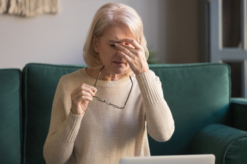 Elderly woman taking off glasses tired of computer work