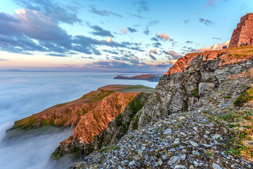 Cliffs of Northern cape of Soroya Island in midnight sun light. Fascinating sea of clouds is...