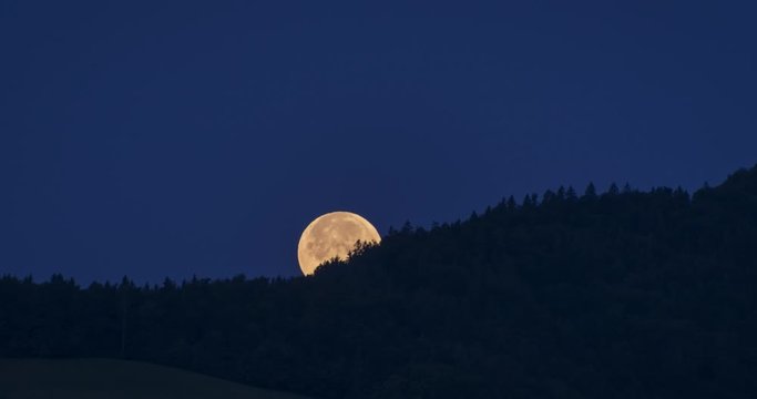 Time lapse of huge yellow moon setting behind a hill during night