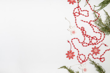 Christmas wooden toys in the form of a white angel and a red snowflake with juniper branches and red beads with space for copy space with a flat lay on a white background.