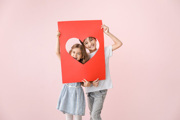 Cute little children holding paper sheet with hole in shape of heart on color background. Valentines Day celebration