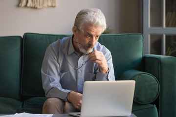 Astonished mature man take off glasses looking at computer screen