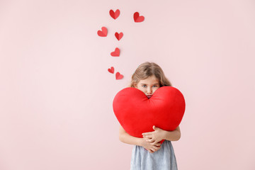 Cute little girl with pillow in shape of heart on color background. Valentines Day celebration