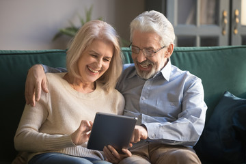 Cheerful elderly spouses having fun using digital tablet