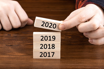 hand holding wooden cube with flip over block 2019 to 2020 word on table background. Resolution,...