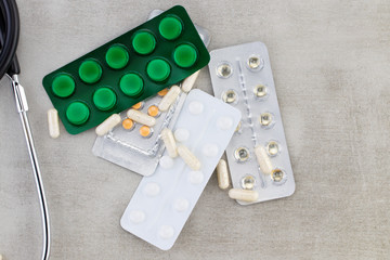  Stethoscope, pills, tablets and capsules on a gray background . Family healthcare, medicine and...