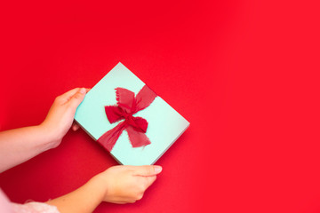 Gift box in woman's hands on a red background. Surprise for Mother's Day, Valentine's Day or Women's Day.
