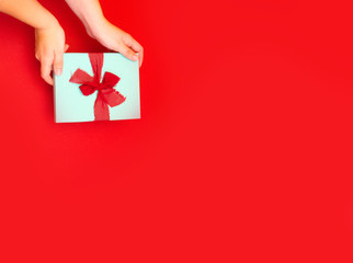 Gift box in woman's hands on a red background. Surprise for Mother's Day, Valentine's Day or Women's Day.