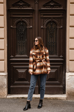 authentic street style portrait of an attractive woman wearing plaid check jacket coat, sunglasses and brown leather bag, crossing the street. fashion outfit details perfect for autumn fall winter