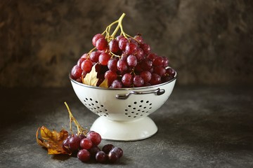 Red grapes in a white colander on a gray background.