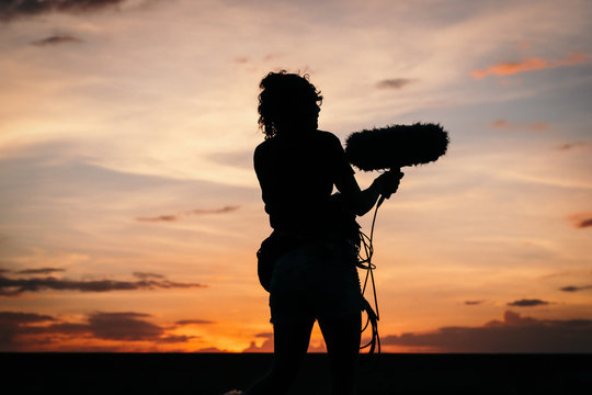 Silhouette of a woman recording sound on a sunset