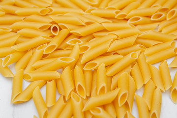 Pasta penne rigate on a white wooden table background. Top view, copy space