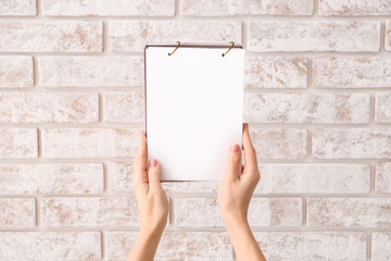 Female hands with blank notebook on brick background