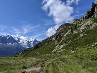 A scenic Alpine view of the famous trek Tour du Mount with sunny blue sky, a few clouds and snowy mountains far away