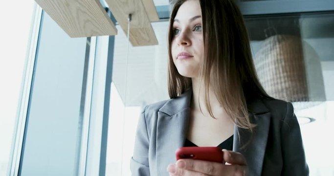 Portrait of young attractive woman looking at smartphone on the office near bif window