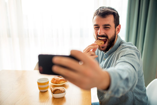 Smiling young man take selfie while eating breakfast