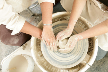 An art teacher teaches a student on a potter's wheel.
