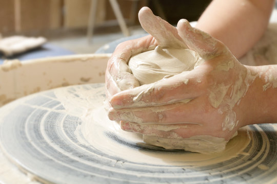 A young person works with clay on a potter's wheel.