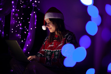 girl student in Christmas clothes sits at home with a laptop at night, a lonely woman meets a holiday online, she use a computer for Christmas