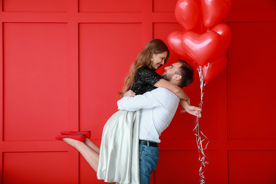 Happy young couple with heart-shaped balloons on color background. Valentine's Day celebration