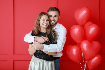 Happy young couple with heart-shaped balloons on color background. Valentine's Day celebration