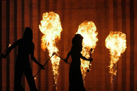 Silhouettes of men and women in the background of a stone wall and burning torches