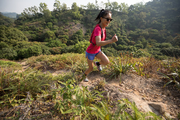 Woman trail runner running up on mountain slope in tropical forest