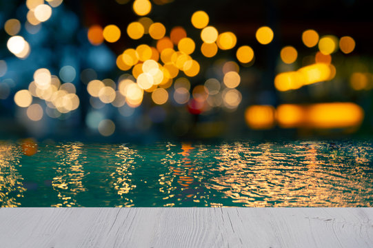 top of white wood table blur bokeh golden orange light swimming pool pool party in the dark night with blue water background