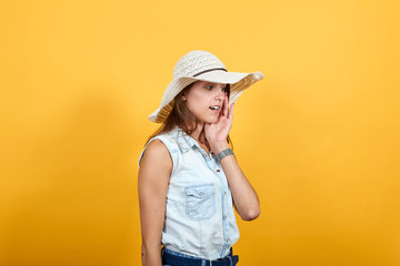 Caucasian young woman in blue denim shirt and fashion hat, keeping hand near mouth, looking shocked isolated on orange background in studio. People sincere emotions, lifestyle concept.